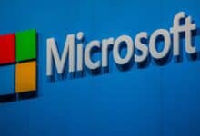 The Microsoft logo displayed on a blue wall, featuring the company name in white letters next to the red, green, blue, and yellow square icon.