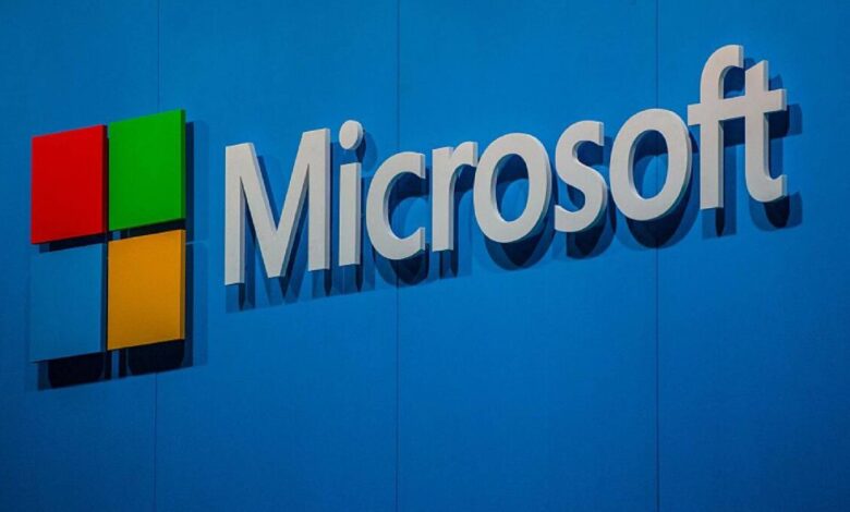 The Microsoft logo displayed on a blue wall, featuring the company name in white letters next to the red, green, blue, and yellow square icon.