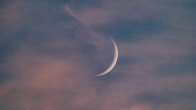 The image of crescent moon glows in a cloudy sky at dusk, with shades of pink, purple, and blue blending across the horizon. Wispy clouds are faintly illuminated, creating a serene and tranquil atmosphere.