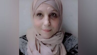The image of of a 66-year-old Palestinian woman wearing a light-coloured hijab and patterned top, looking slightly upward with a calm expression.