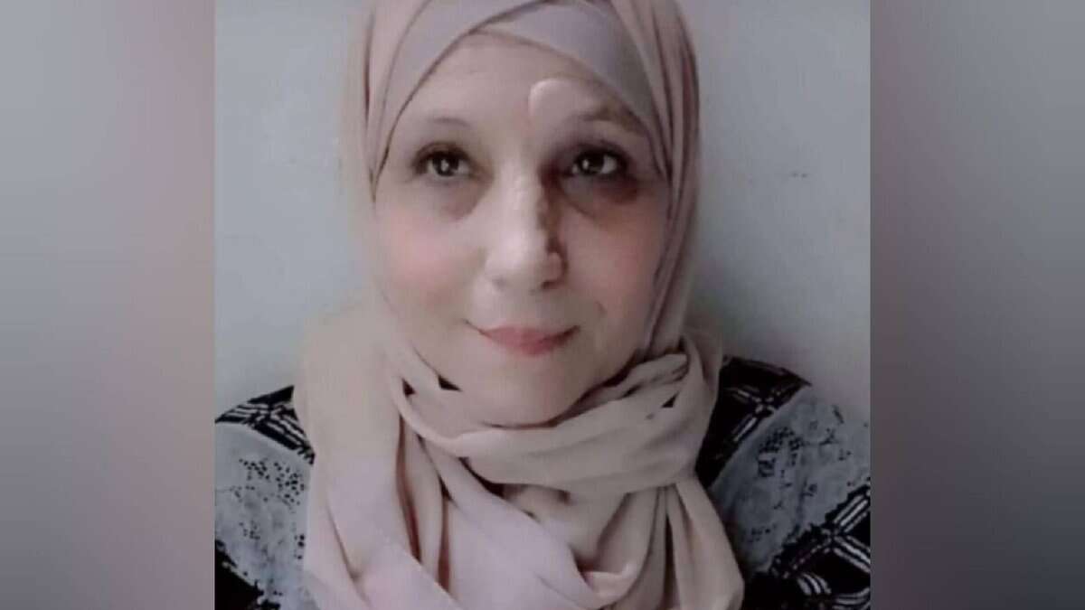 The image of of a 66-year-old Palestinian woman wearing a light-coloured hijab and patterned top, looking slightly upward with a calm expression.