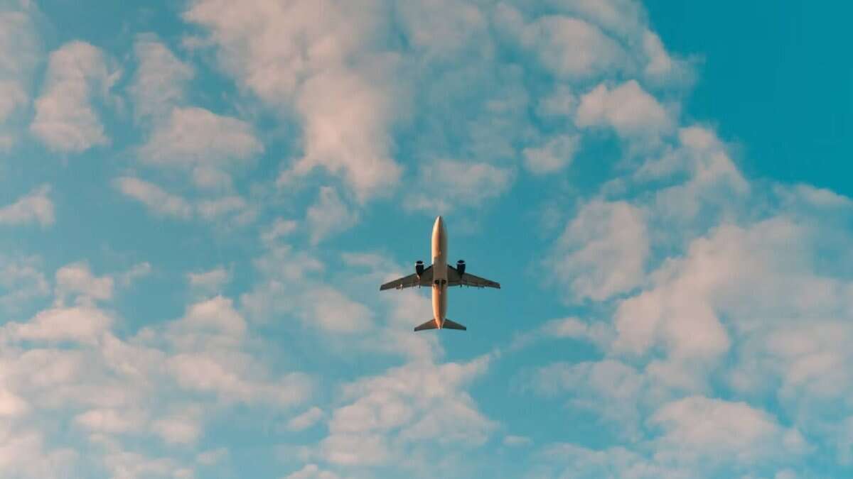 An aeroplane flying overhead against a blue sky with scattered white clouds.