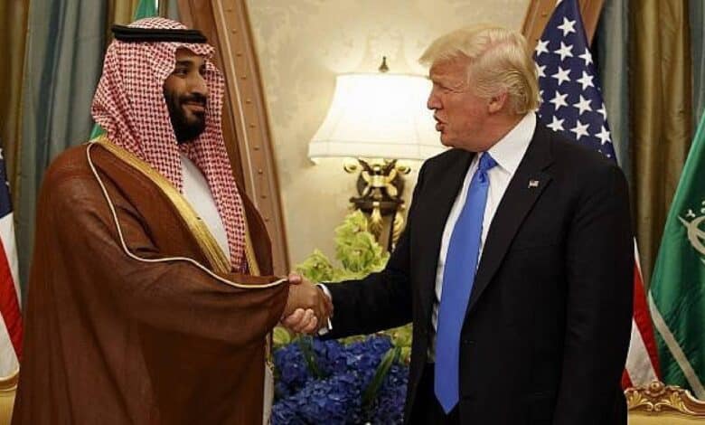 The image of Saudi Crown Prince Mohammed bin Salman shakes hands with US President Donald Trump during a meeting, with Saudi and US flags in the background.
