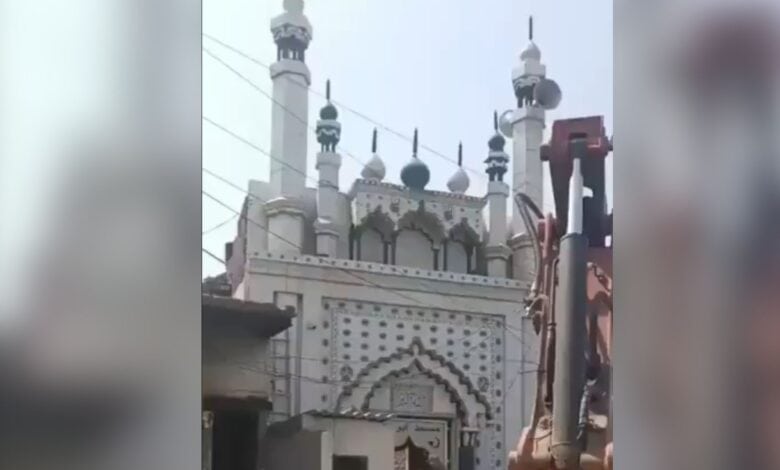 The image displays a Faridabad authorities trying to demolish a local mosque wall