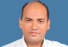 The image of of Aju Paul, an Indian man wearing a white shirt, posing against a plain blue background.