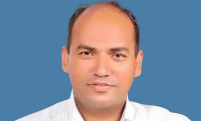 The image of of Aju Paul, an Indian man wearing a white shirt, posing against a plain blue background.