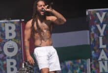 Shirtless rapper Bob Vylan performs on stage at Glastonbury Festival, with a Palestinian flag and colourful set decorations in the background.