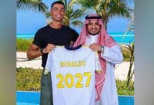 The image of Cristiano Ronaldo stands beside an Al Nassr official on a tropical beach, holding a football jersey with his name and "2027" printed on the back, celebrating his contract extension.