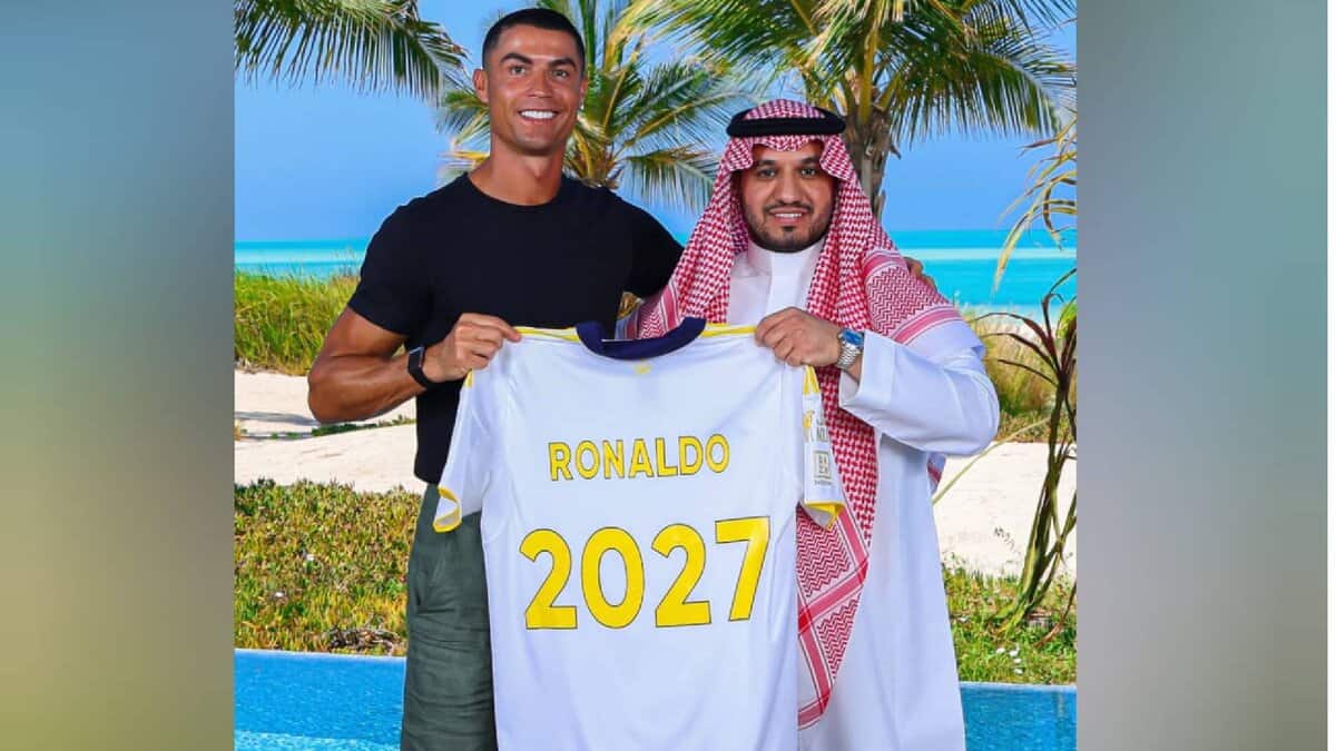 The image of Cristiano Ronaldo stands beside an Al Nassr official on a tropical beach, holding a football jersey with his name and