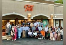 A large group of men and women pose together outside FiLLi Cafe in Villa Park, Illinois, during the DAANA mentorship event. The café's exterior features the orange FiLLi sign above, with attendees dressed in a mix of formal and semi-formal attire.