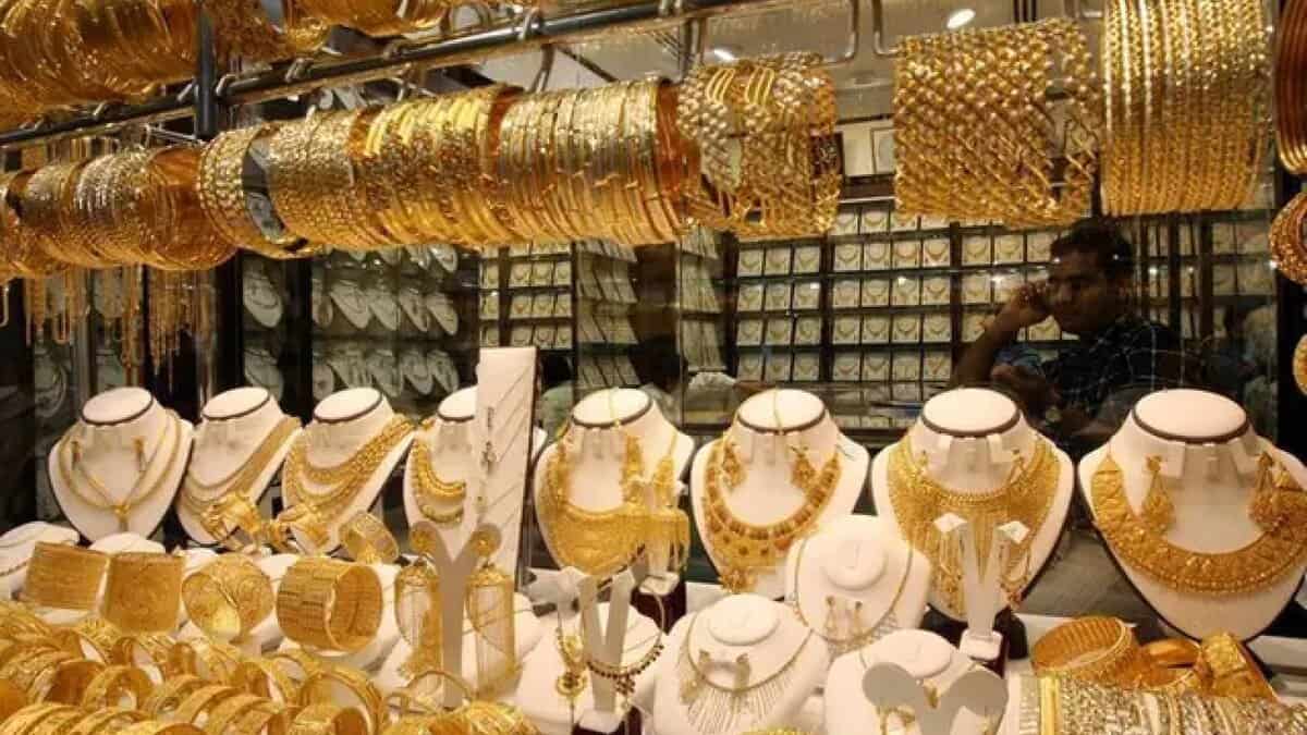 Gold jewellery shop in Dubai Gold Souk showcasing ornate bangles, necklaces and sets; shopkeeper visible in background.