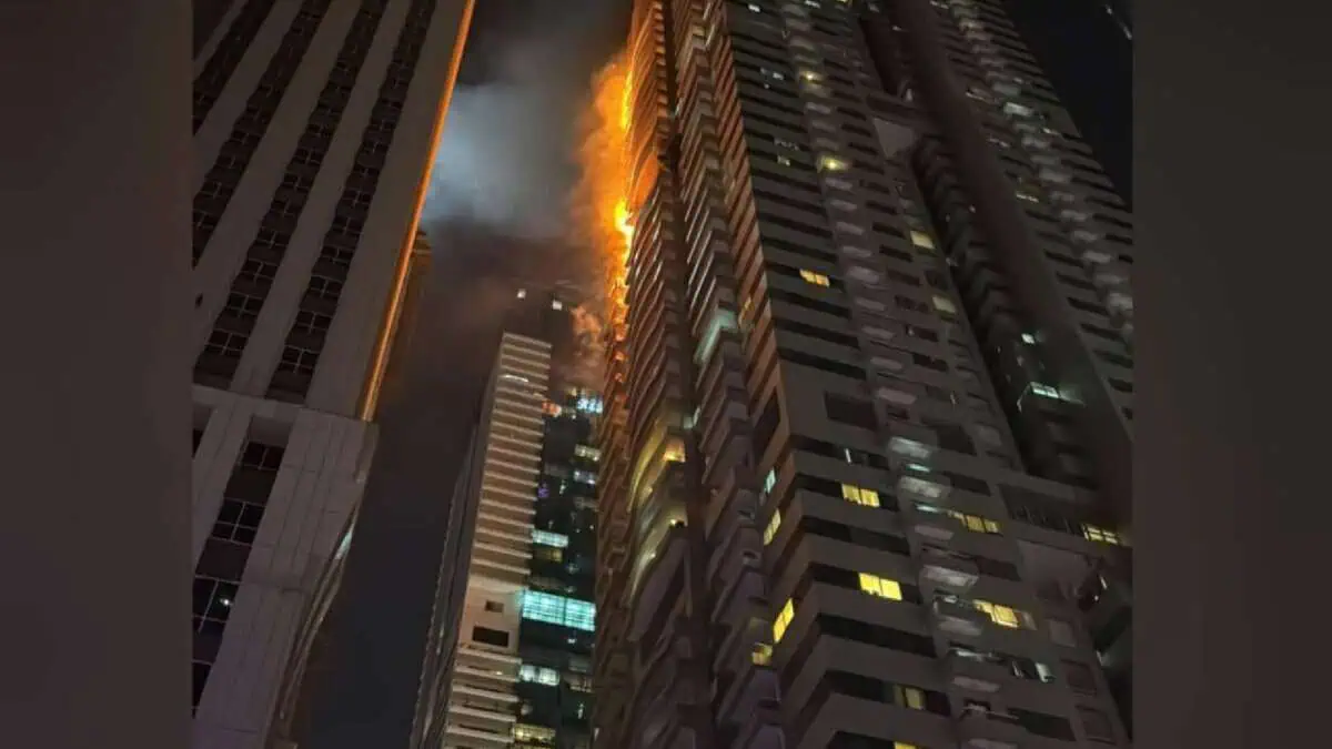 Flames and smoke rise from the upper floors of a high-rise residential tower at night in Dubai Marina, with neighbouring buildings visible in the foreground.