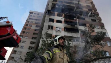 A firefighter gestures at the site of a damaged residential building in northern Tehran, with smoke rising from the upper floors after Israeli strikes.
