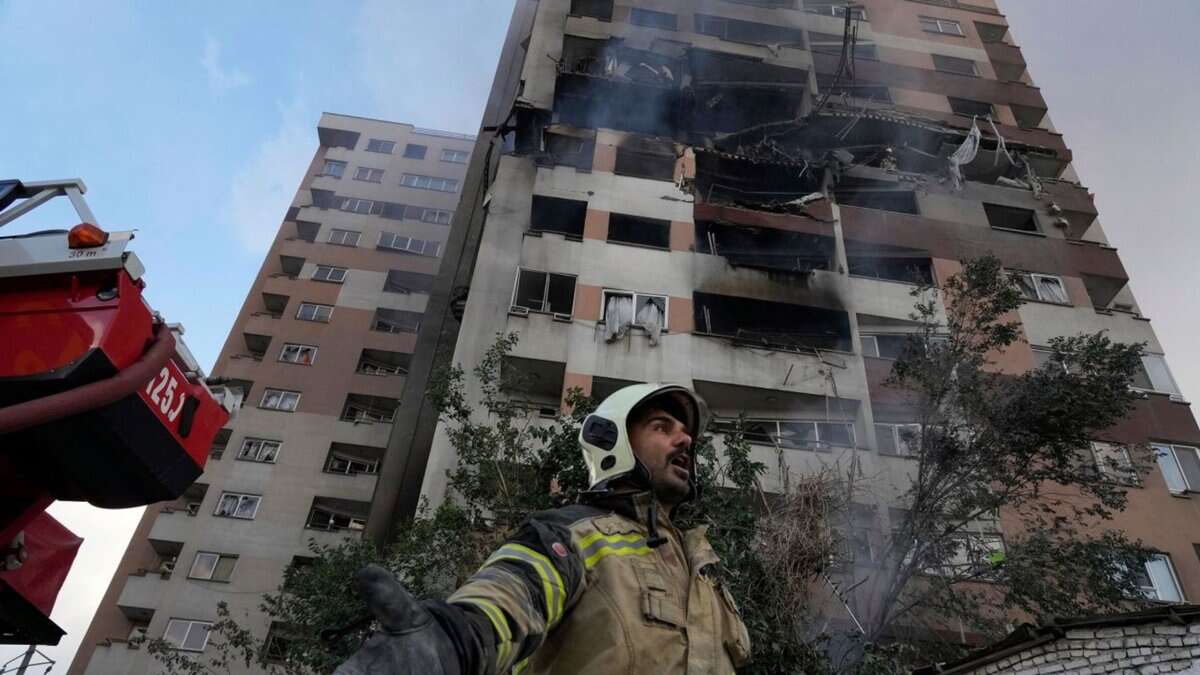 A firefighter gestures at the site of a damaged residential building in northern Tehran, with smoke rising from the upper floors after Israeli strikes.