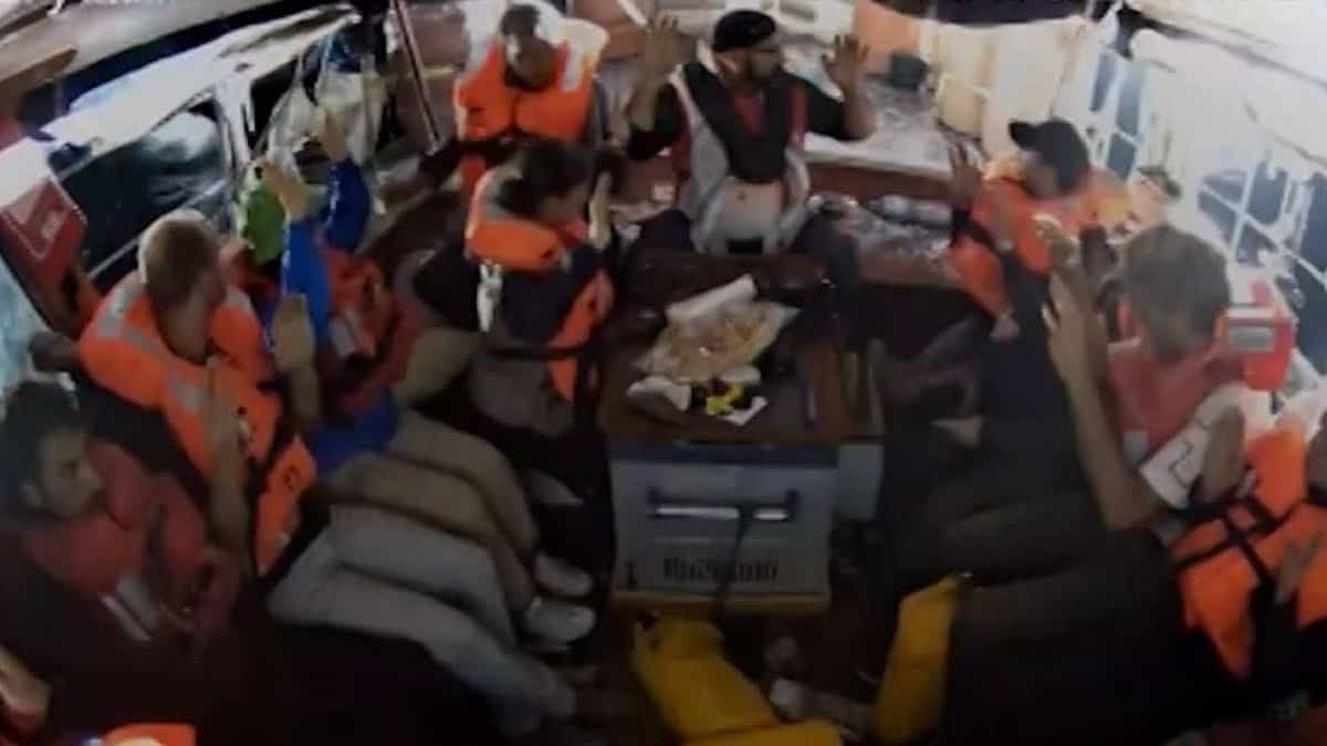Crew members of a Gaza-bound aid ship wearing life jackets sit closely together with hands raised inside the vessel after being detained by Israeli forces.