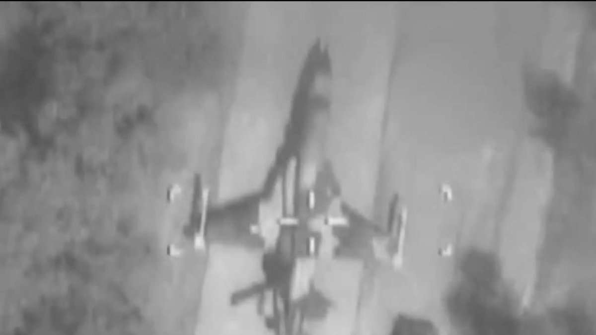 Infrared aerial view showing an Iranian F-5 fighter jet parked on the runway at Dezful Airport, moments before an Israeli airstrike. The black-and-white image captures the aircraft from above, surrounded by trees and concrete.