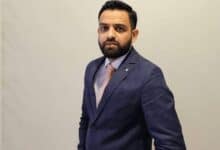 The image of a Indian banker Mustafa Mohammed wearing a navy blue suit and peach-striped tie poses confidently against a plain beige background.