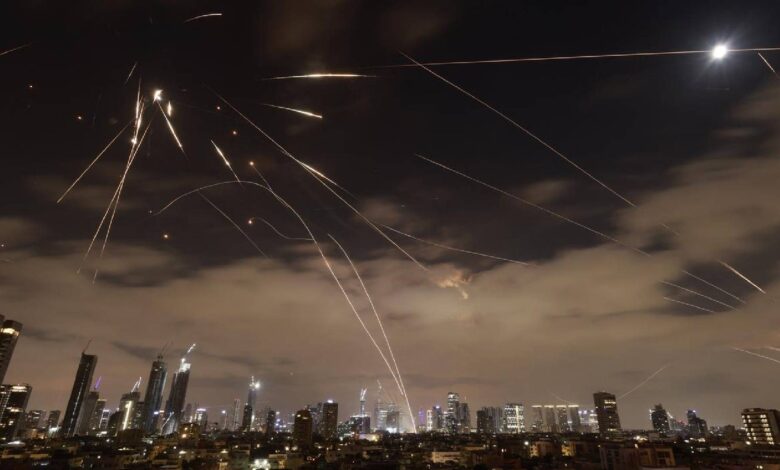 The image of a Israeli air defence systems intercepting Iranian missiles over Tel Aviv at night, with bright trails of interceptor rockets lighting up the sky above the city skyline.