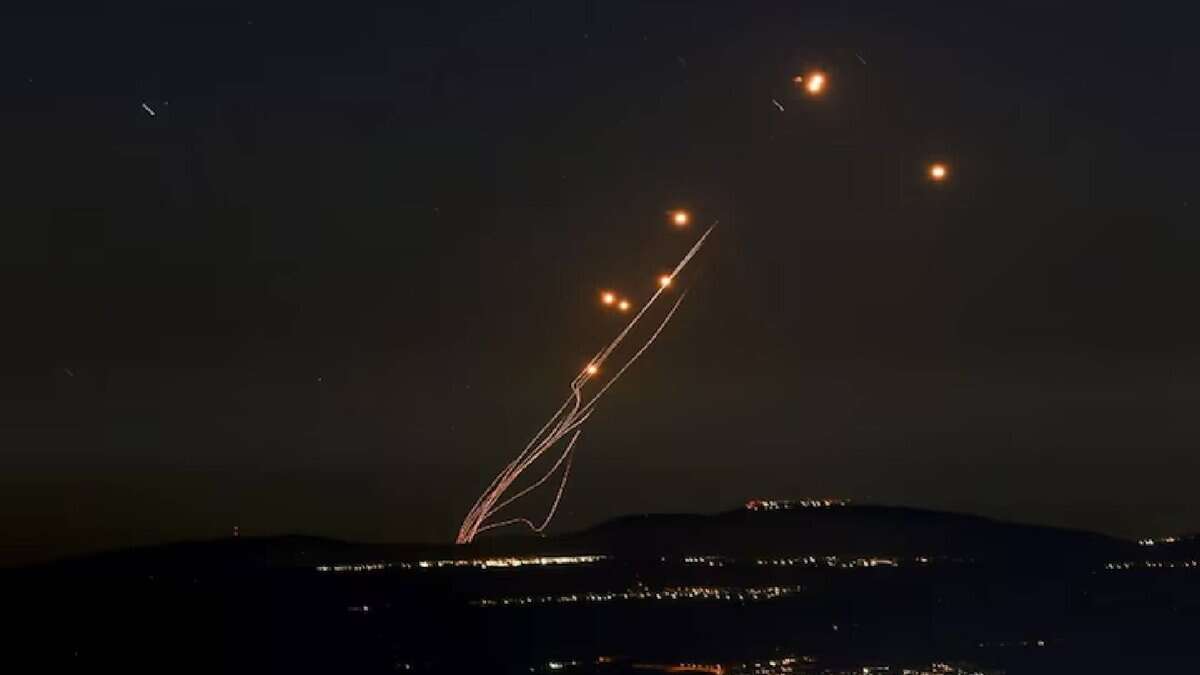 Israel’s Iron Dome missile defence system launches an interceptor during an incoming rocket attack, with smoke trails visible against the evening sky.