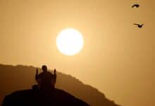 Pilgrim praying at dawn on Mount Arafat during Haj pilgrimage in Saudi Arabia, with sunrise in the background.