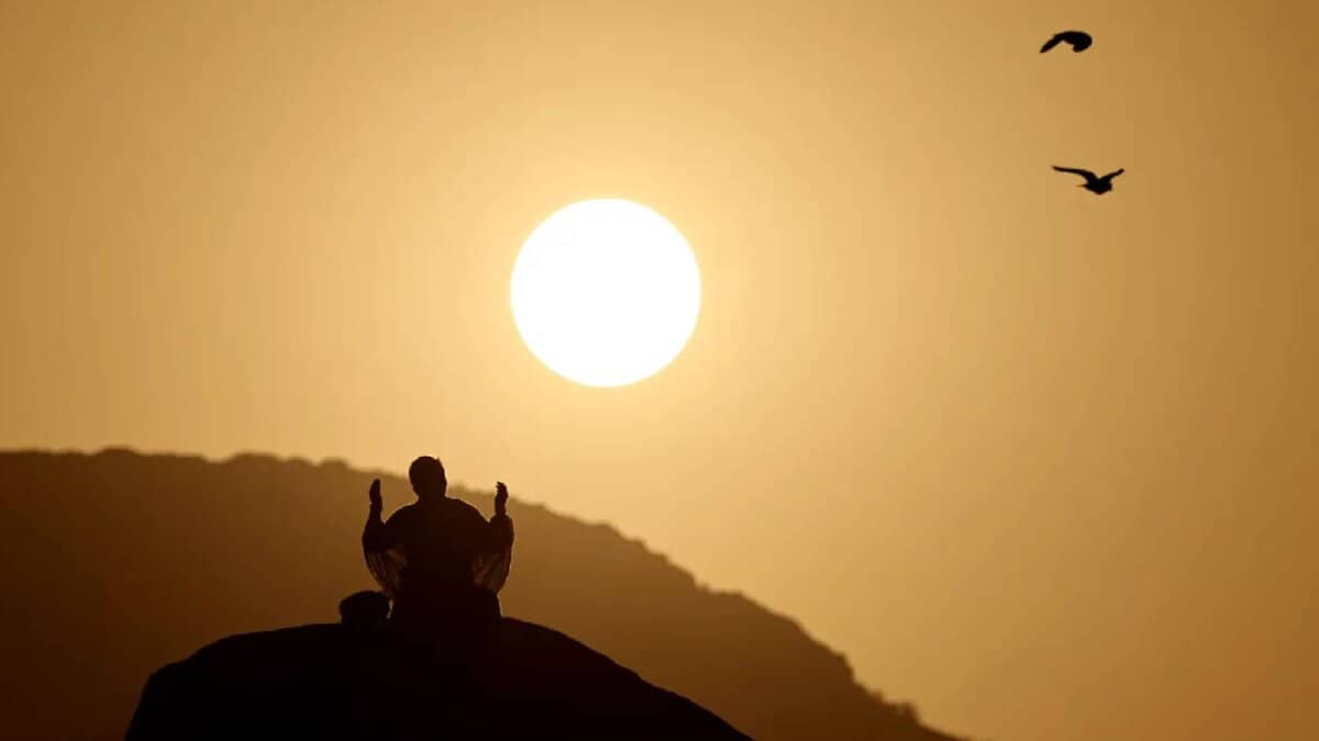 Pilgrim praying at dawn on Mount Arafat during Haj pilgrimage in Saudi Arabia, with sunrise in the background.