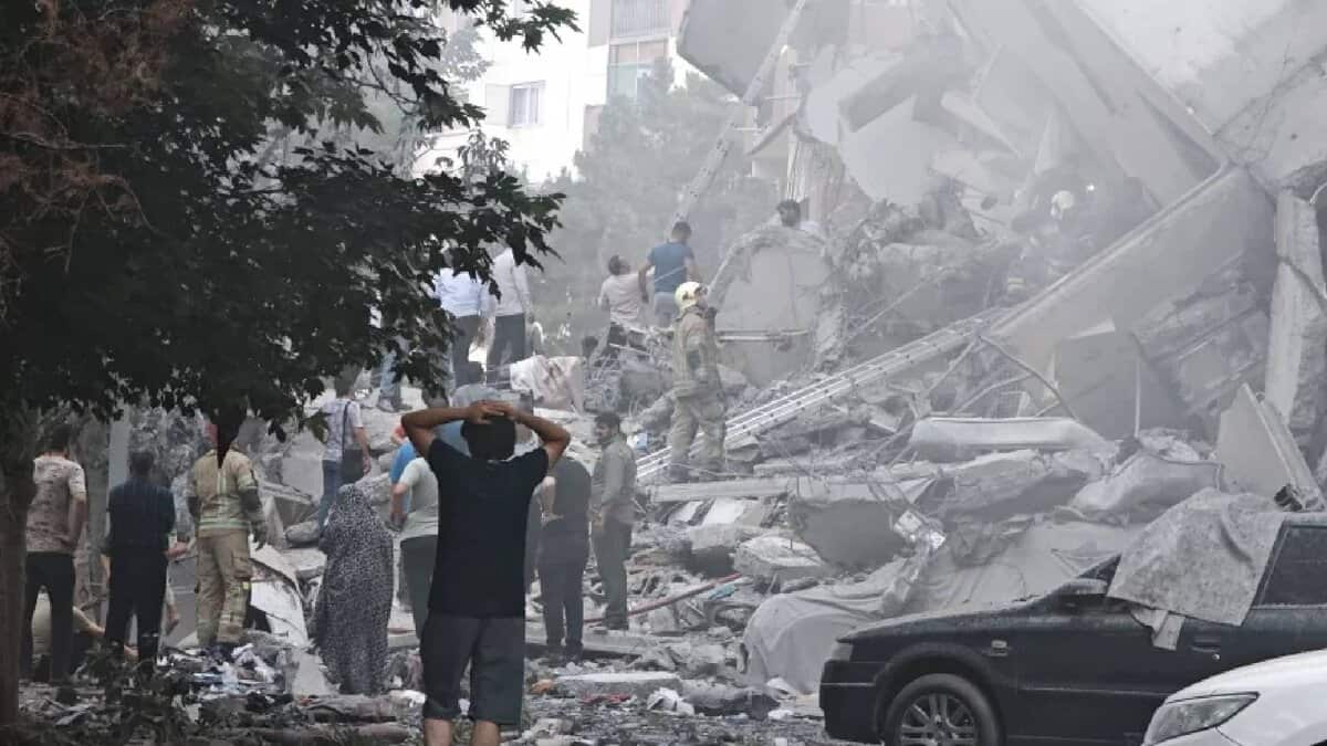 People search through rubble and damaged vehicles after a building collapsed in Tehran, Iran. The area is filled with dust and debris as rescuers and civilians gather at the scene of destruction caused by airstrikes.