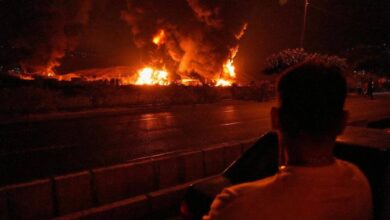 The image of a man watches massive flames and thick smoke rise from an oil storage facility in Tehran after it was struck by an Israeli missile early on June 15.