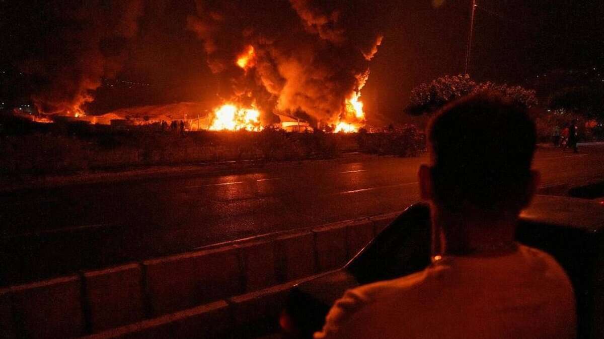 The image of a man watches massive flames and thick smoke rise from an oil storage facility in Tehran after it was struck by an Israeli missile early on June 15.