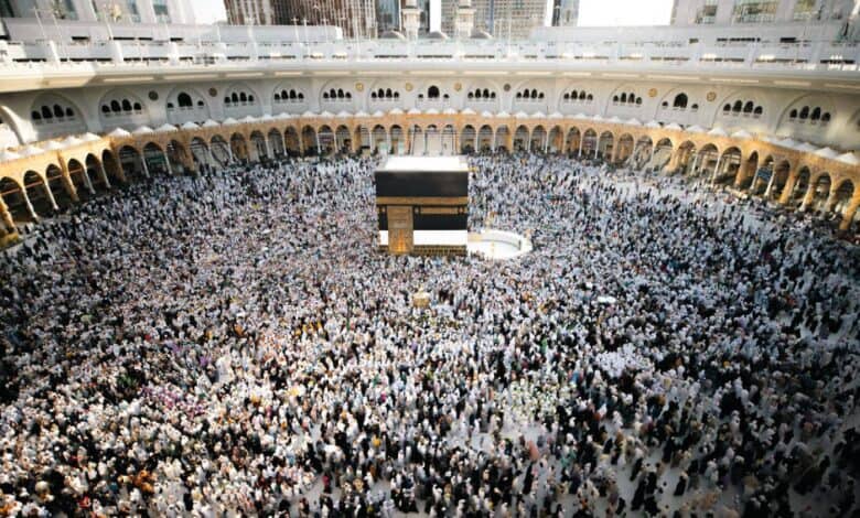 A large crowd of pilgrims gathers around the Kaaba inside the Masjid al-Haram in Makkah during Umrah. The mosque’s white marble flooring and arched colonnades surround the central black-draped structure as worshippers perform tawaf.