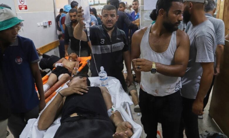 Palestinians wounded while returning from a Gaza Humanitarian Foundation aid centre lie on stretchers and are treated by others inside Nasser Hospital in Khan Younis. The crowded emergency room shows visible signs of distress, with injured individuals receiving IV fluids and first aid.