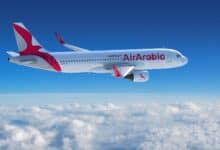 The image of Air Arabia Airbus A320 aircraft flying above the clouds with a clear blue sky in the background.