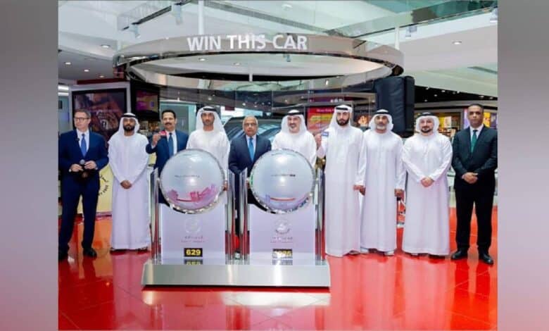 Group photo at Dubai Duty Free draw held at Concourse A, Dubai International Airport, with officials standing beside raffle drums.