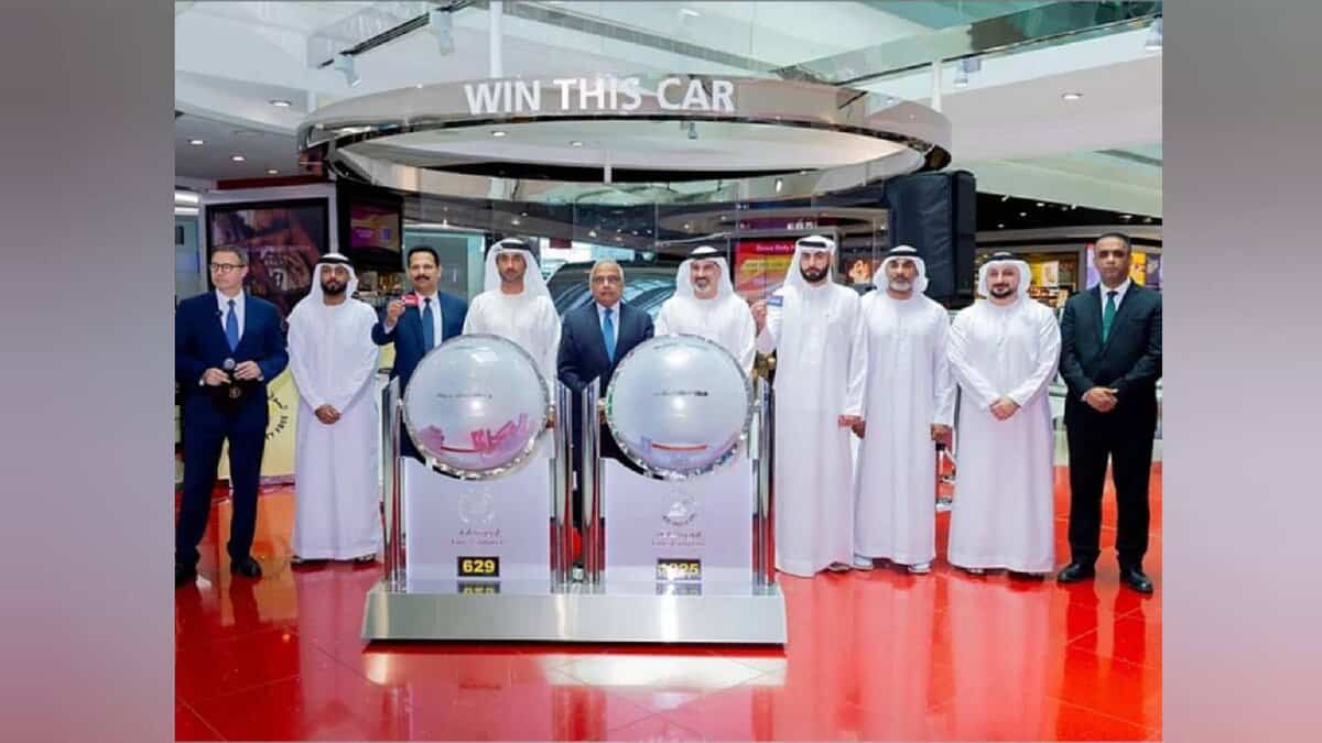Group photo at Dubai Duty Free draw held at Concourse A, Dubai International Airport, with officials standing beside raffle drums.