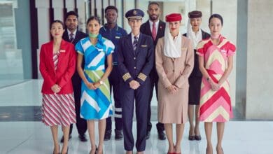 A group of Emirates airline staff in diverse uniforms standing together in a modern indoor setting.