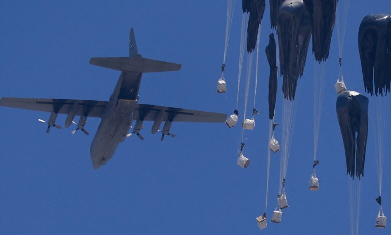 A military airplane in flight dropping humanitarian aid packages with parachutes over a clear blue sky, viewed from the northern Gaza Strip.