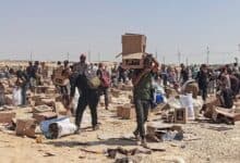 The image of people gather at a Gaza aid distribution site, collecting boxes and supplies scattered across a dusty, open area under the sun.