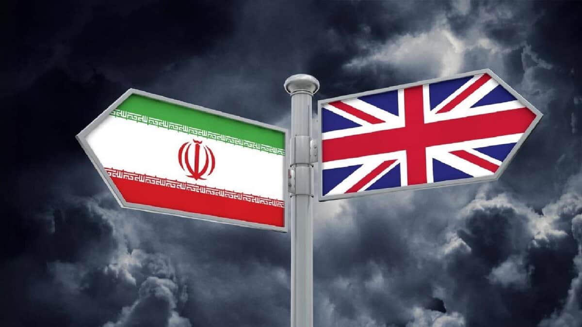 A signpost with two directional arrows, one displaying the Iranian flag on the left and the other the United Kingdom flag on the right, set against a dark, stormy cloud background.