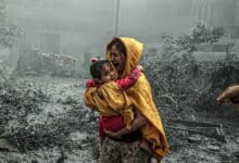The image of a distressed woman in a yellow shawl carries a frightened child through rubble-filled streets after an Israeli airstrike in Gaza City.