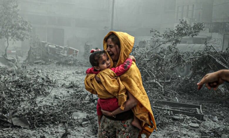 The image of a distressed woman in a yellow shawl carries a frightened child through rubble-filled streets after an Israeli airstrike in Gaza City.