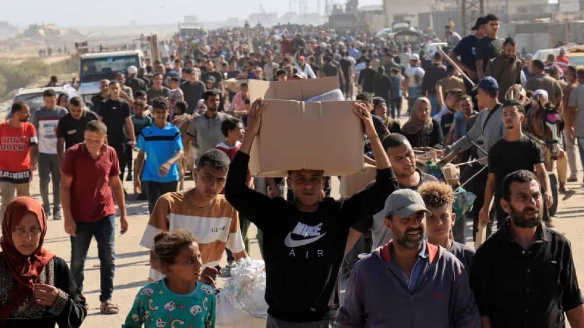 A large crowd of Palestinians, including men, women, and children, gathers near an aid distribution site in Rafah, southern Gaza Strip, with some holding boxes and bags of supplies.