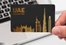 A hand holding a black UAE Golden Visa card with gold-colored silhouettes of iconic buildings, including the Burj Al Arab and Burj Khalifa, set against a laptop keyboard in the background.