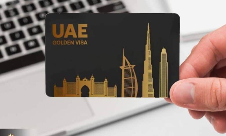 A hand holding a black UAE Golden Visa card with gold-colored silhouettes of iconic buildings, including the Burj Al Arab and Burj Khalifa, set against a laptop keyboard in the background.