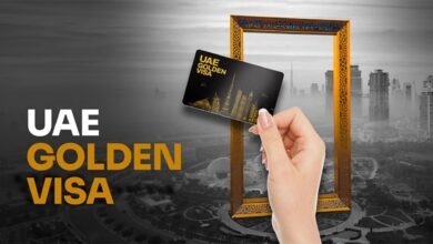 Hand holding UAE Golden Visa card in front of Dubai Frame skyline.