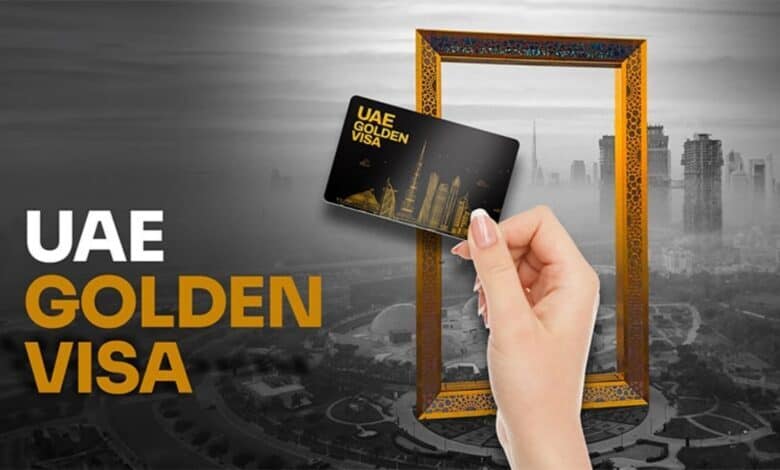 Hand holding UAE Golden Visa card in front of Dubai Frame skyline.