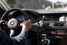 Close-up of hands on the steering wheel of a BMW while driving on a clear road.