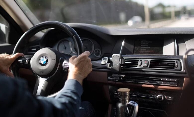 Close-up of hands on the steering wheel of a BMW while driving on a clear road.