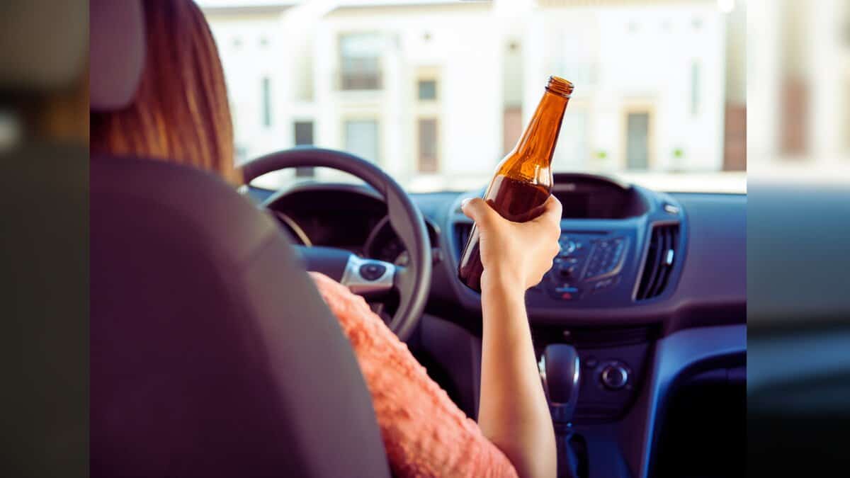 A woman driving with a bottle in hand
