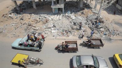 Displaced Palestinians travel in vehicles past buildings reduced to rubble in Gaza, amid ongoing conflict and destruction.