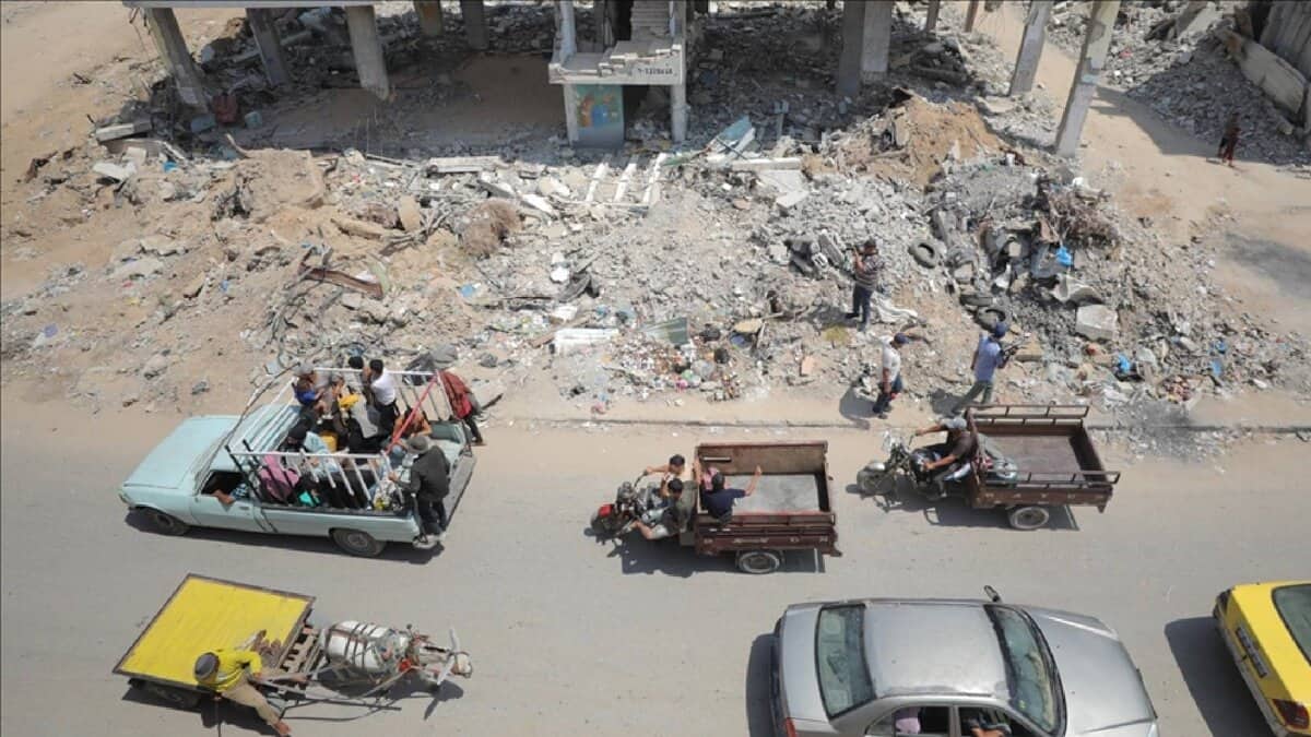 Displaced Palestinians travel in vehicles past buildings reduced to rubble in Gaza, amid ongoing conflict and destruction.