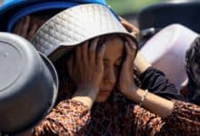 A Palestinian girl, with a cooking pot on her head for shade, rests her face in her hands while waiting in a long queue to receive food in Gaza City.